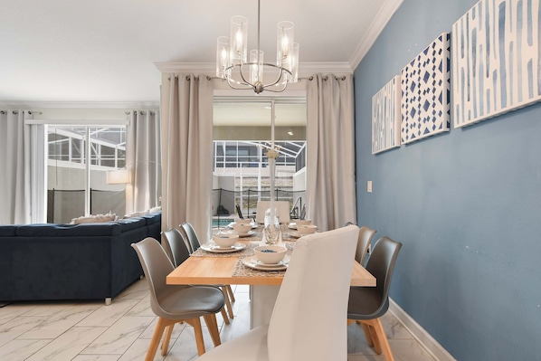 A dining area with a table set for four, a chandelier, and a view of a pool and outdoor area.