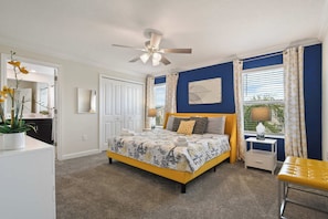 A bedroom with a bed, a nightstand, a chair, a ceiling fan, and a window with curtains.