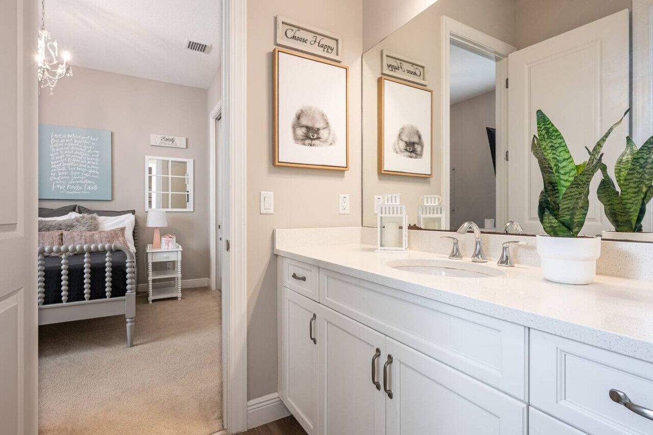 A bathroom with a double sink vanity, a chandelier, framed artwork, and a potted plant.