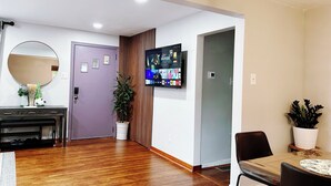 A modern living room with a wooden floor, a round mirror, a flat-screen TV mounted on the wall, a dining area with a table and chairs, and a potted plant. - Comfy 3Bedrooms 2Bathrooms Excellent Location Home near to Downtown Pittsburgh (Pittsburgh)