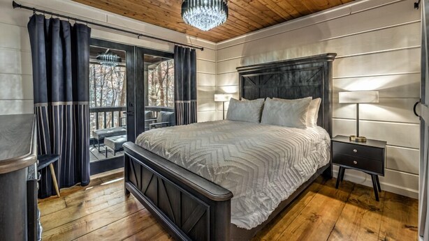 Une chambre à coucher avec un grand lit, une table de chevet, une fenêtre avec des rideaux et un lustre.
