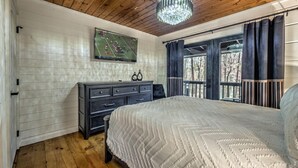 Une chambre avec un plafond en bois, un grand lit recouvert d’une couette blanche, une commode et une décoration murale sur le thème du sport.