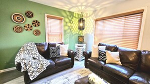 Una sala de estar con dos sofás de cuero, una manta decorativa estampada, una alfombra decorativa y cuadros en la pared.