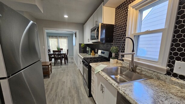 Una cocina moderna con electrodomésticos de acero inoxidable, encimera de granito y salpicadero hexagonal blanco y negro.