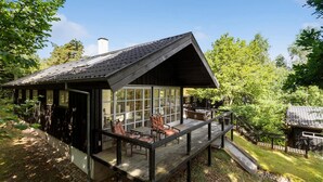 A cabin with a deck, large windows, and a chimney.