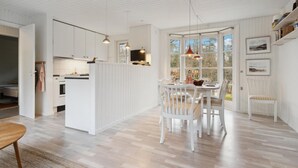 A spacious kitchen with white cabinetry, a dining area with a white table and chairs, and large windows providing natural light.