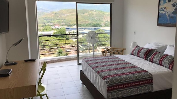 Ein Schlafzimmer mit einem Bett, einem Schreibtisch und einem Stuhl. Es gibt einen Balkon mit Blick auf eine Landschaft.