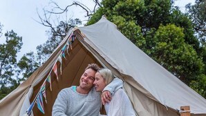 A couple sitting on wooden steps outside a tent with a number '9' sign.