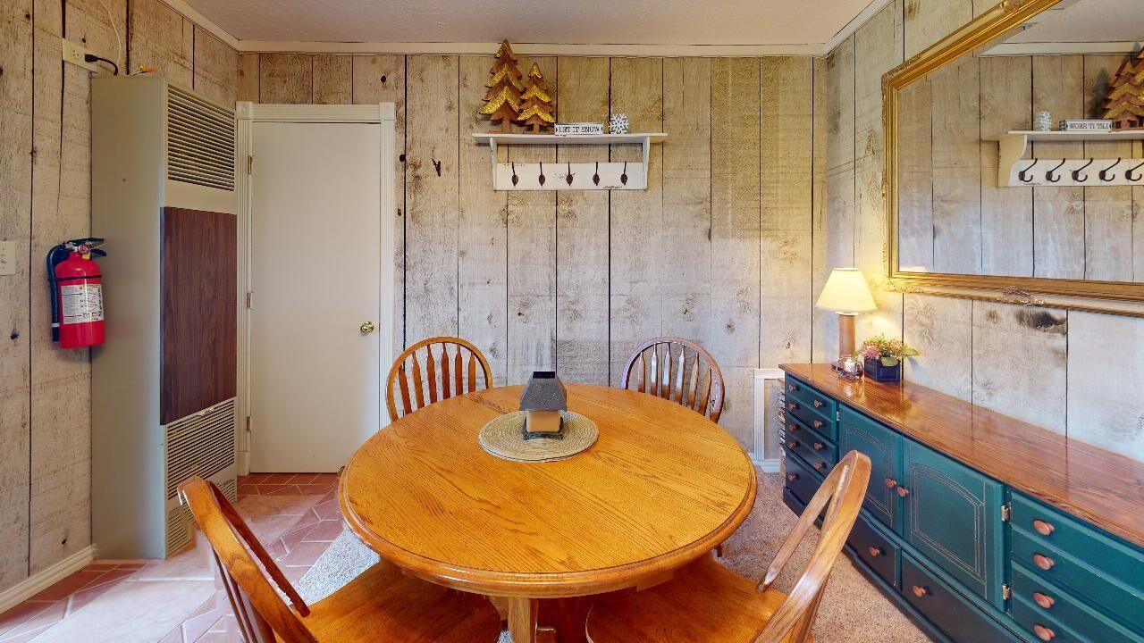 A dining room with a wooden table and chairs, a fire extinguisher, a cabinet with drawers, and a mirror on the wall.