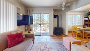 A living room with a sofa, TV, fireplace, dining area, and a view through the glass door.