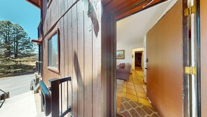 A wooden building with a balcony, a door leading to a room with a sofa and a painting, and a tiled floor. - Close to Lifts | WIFI | Easy Access | Angel Fire Chalet 5 (Angel Fire)