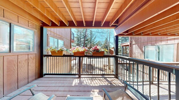 A wooden deck with a railing, potted plants, and a view of trees and buildings. - Close to Lifts | WIFI | Easy Access | Angel Fire Chalet 5 (Angel Fire)