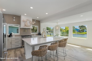 A modern kitchen with a large island, bar stools, and a view of a lake.