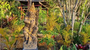 Una estatua de piedra de una criatura mítica en un jardín con diversas plantas tropicales.