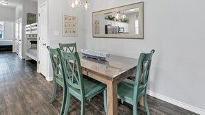 A dining area with a wooden table, green chairs, a large mirror, and a kitchen visible in the background. - Free Sail in Port Aransas! (Port Aransas)