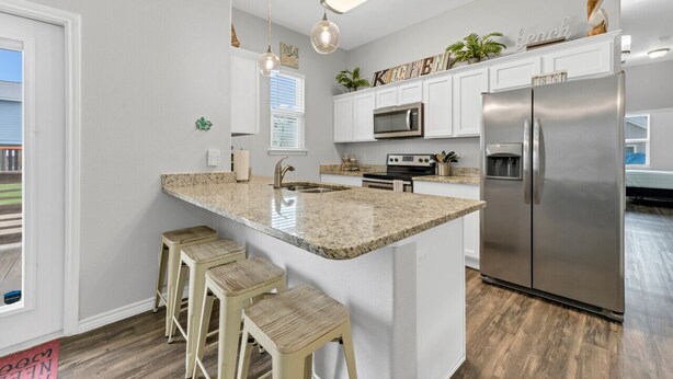 A modern kitchen with white cabinets, a stainless steel refrigerator, granite countertops, and pendant lighting. - Free Sail in Port Aransas! (Port Aransas)