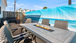 An outdoor patio with a fire pit table, wicker chairs, and a view of the ocean. - Free Sail in Port Aransas! (Port Aransas)