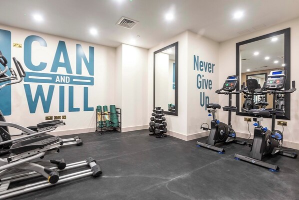Una palestra con decorazioni motivazionali a parete, attrezzature per esercizi e uno specchio.