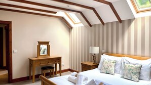 Un dormitorio con tragaluz, cama con almohadas y toallas, mesita de noche, escritorio con espejo y papel tapiz a rayas.