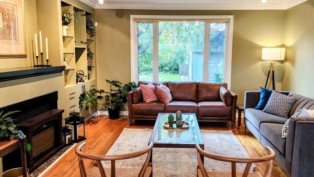 A living room with a brown leather sofa, a grey sofa, a coffee table, and a fireplace. There are plants and a lamp in the room.