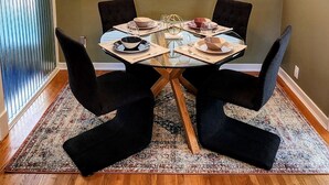 A dining area with a round table, black chairs, a chandelier, and a window with blinds.