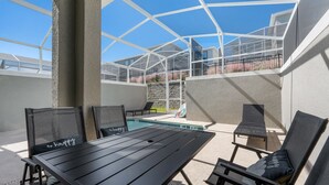 En udendørs terrasse med pool, siddeområde og en tilbygning med glas.