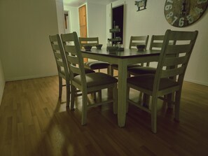 A dining table with four chairs, a wooden floor, and a wall clock.