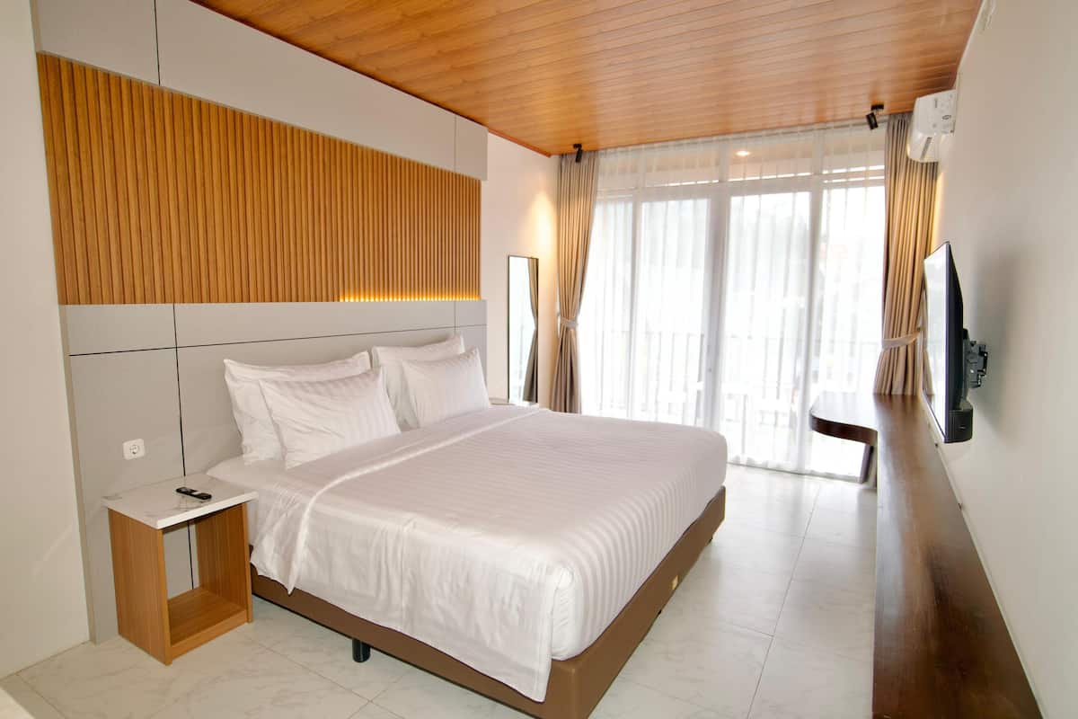 A modern hotel room with a large bed, a wooden headboard, a bedside table, and a TV mounted on the wall.