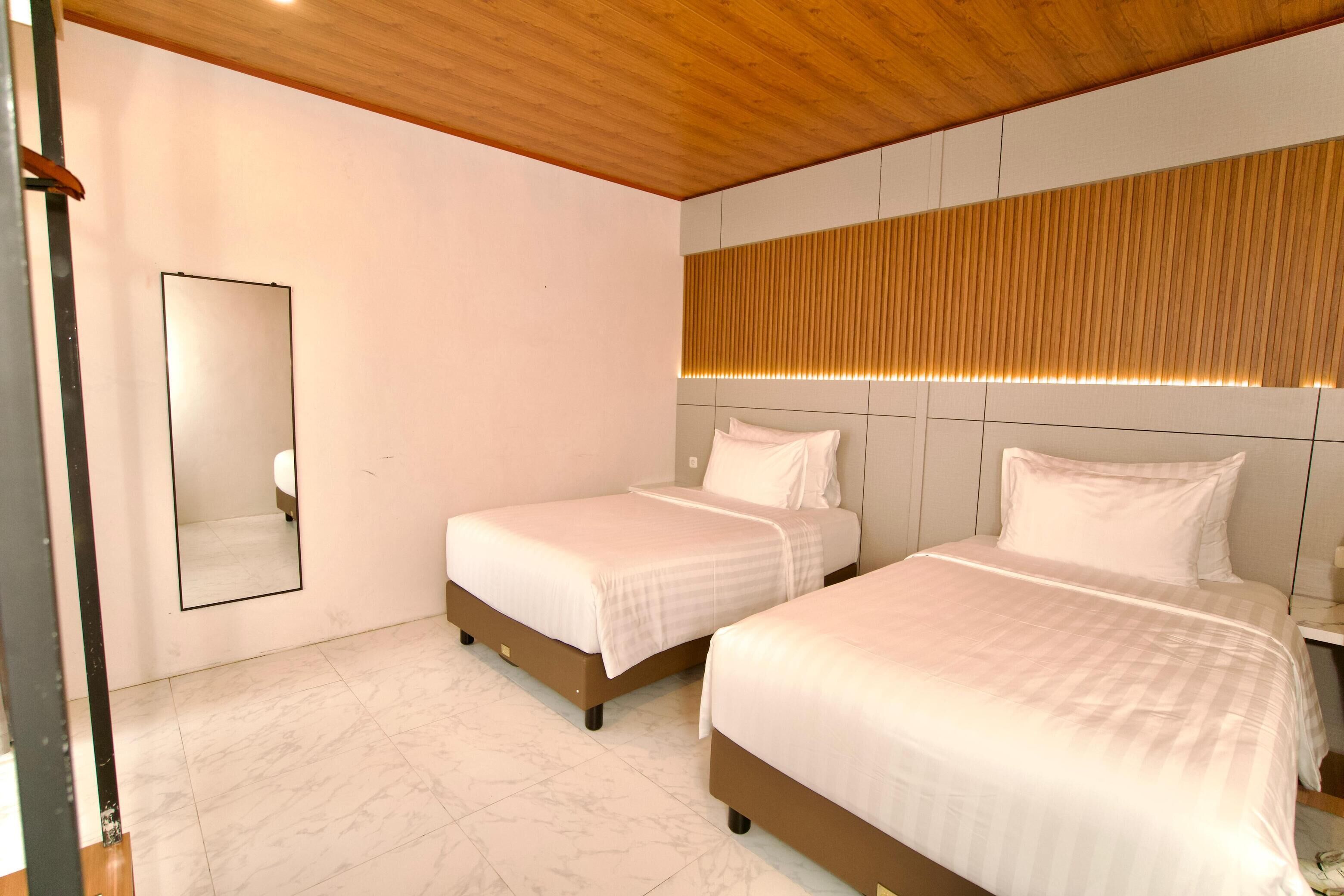 Een hotelkamer met twee bedden, een houten plafond, een grote spiegel en een verlicht paneel aan de muur.