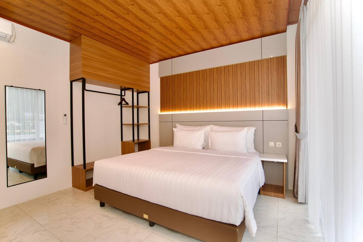 A modern bedroom with a large bed, a wooden ceiling, a bedside table, and a mirror.