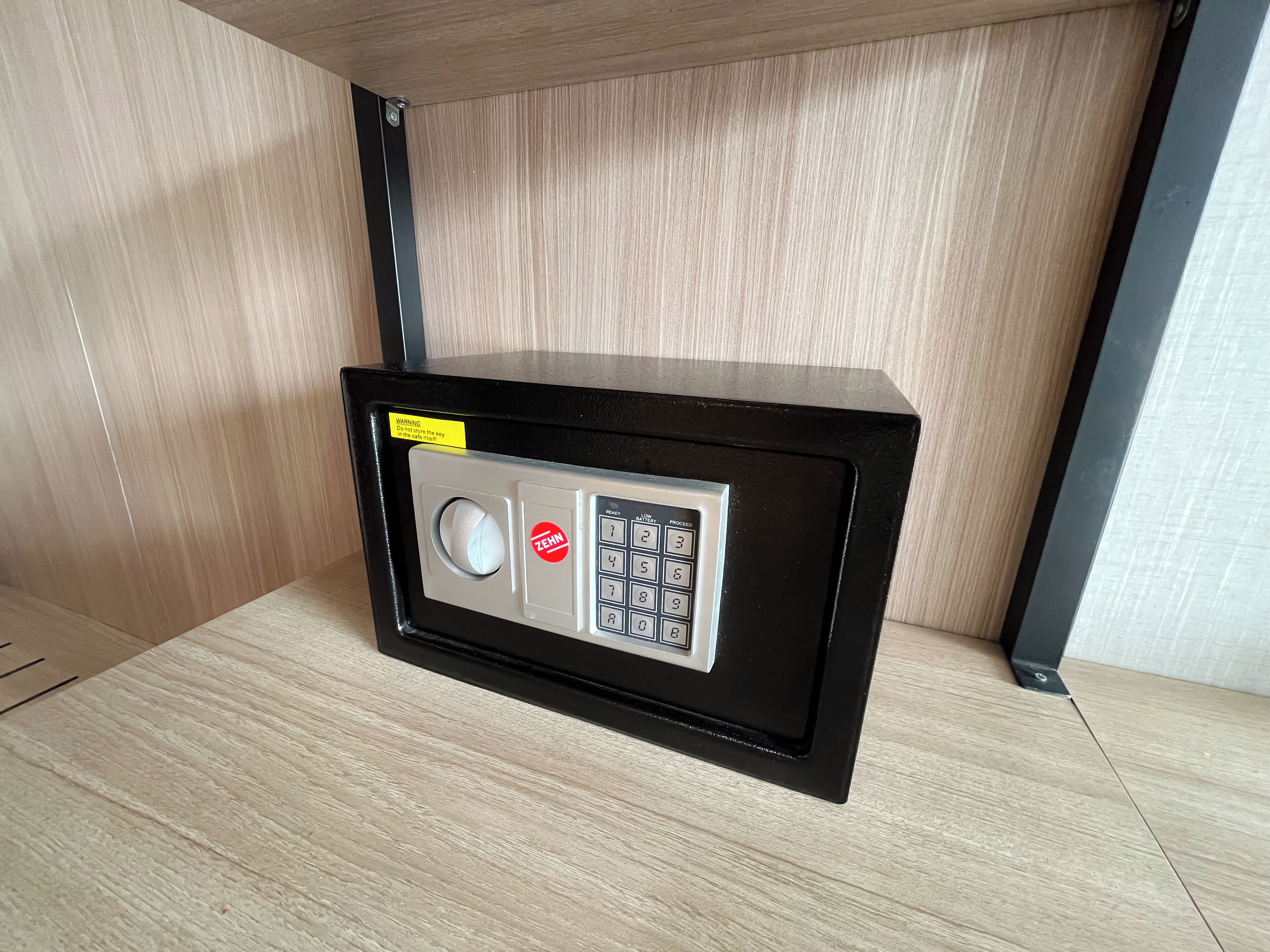 Een zwarte kluis met een keypad en een waarschuwingsticker op een houten vloer.