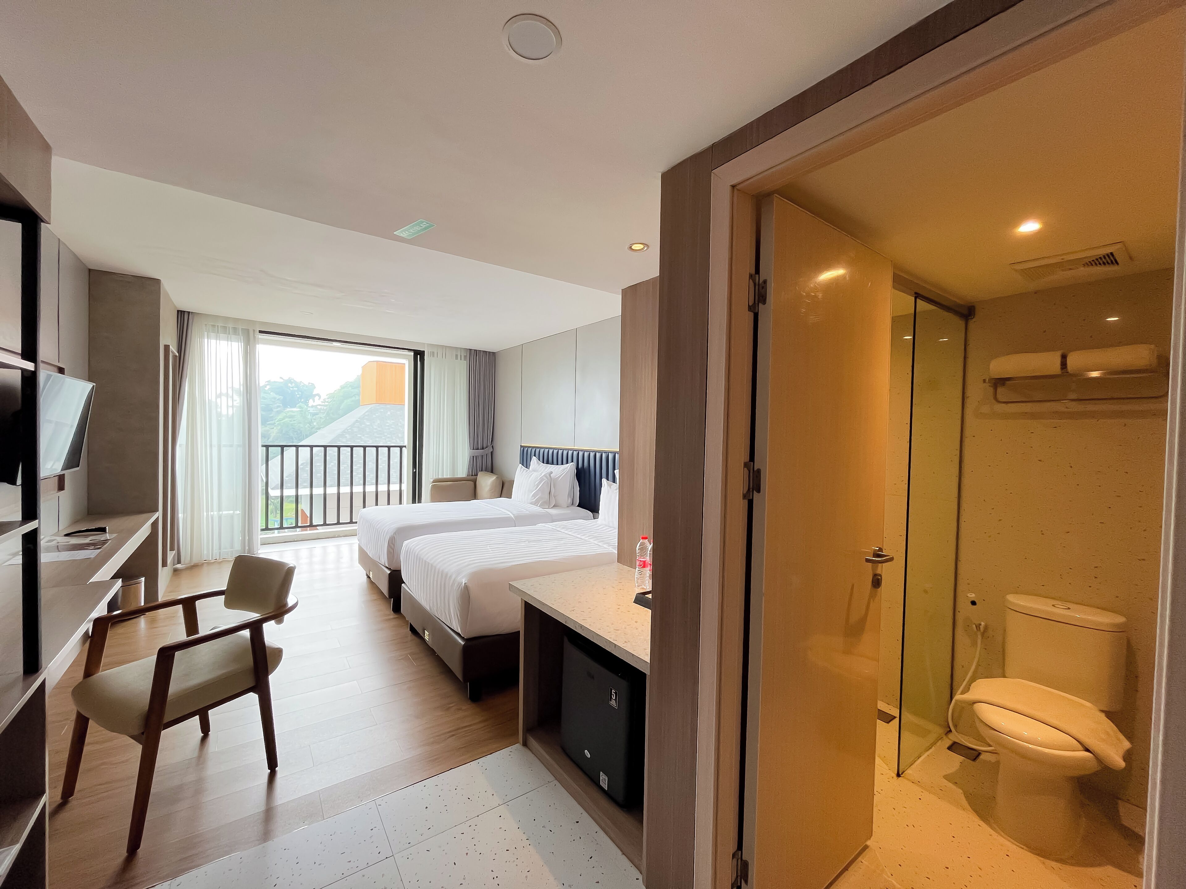 Habitación de hotel con cama, escritorio, silla, televisor, balcón y baño.