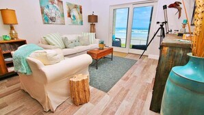 A living room with a white sofa, a coffee table, and a view of the ocean through a glass door.