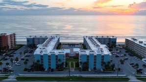 A hotel with a central courtyard, multiple floors, and a view of the ocean at sunset.