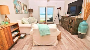 A living room with a sofa, a wooden cabinet, a television, and a view of the ocean through a sliding door.