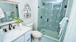 Un bany amb un lavabo blanc, un vàter, una dutxa amb envàs de vidre i un mirall amb marc decoratiu.