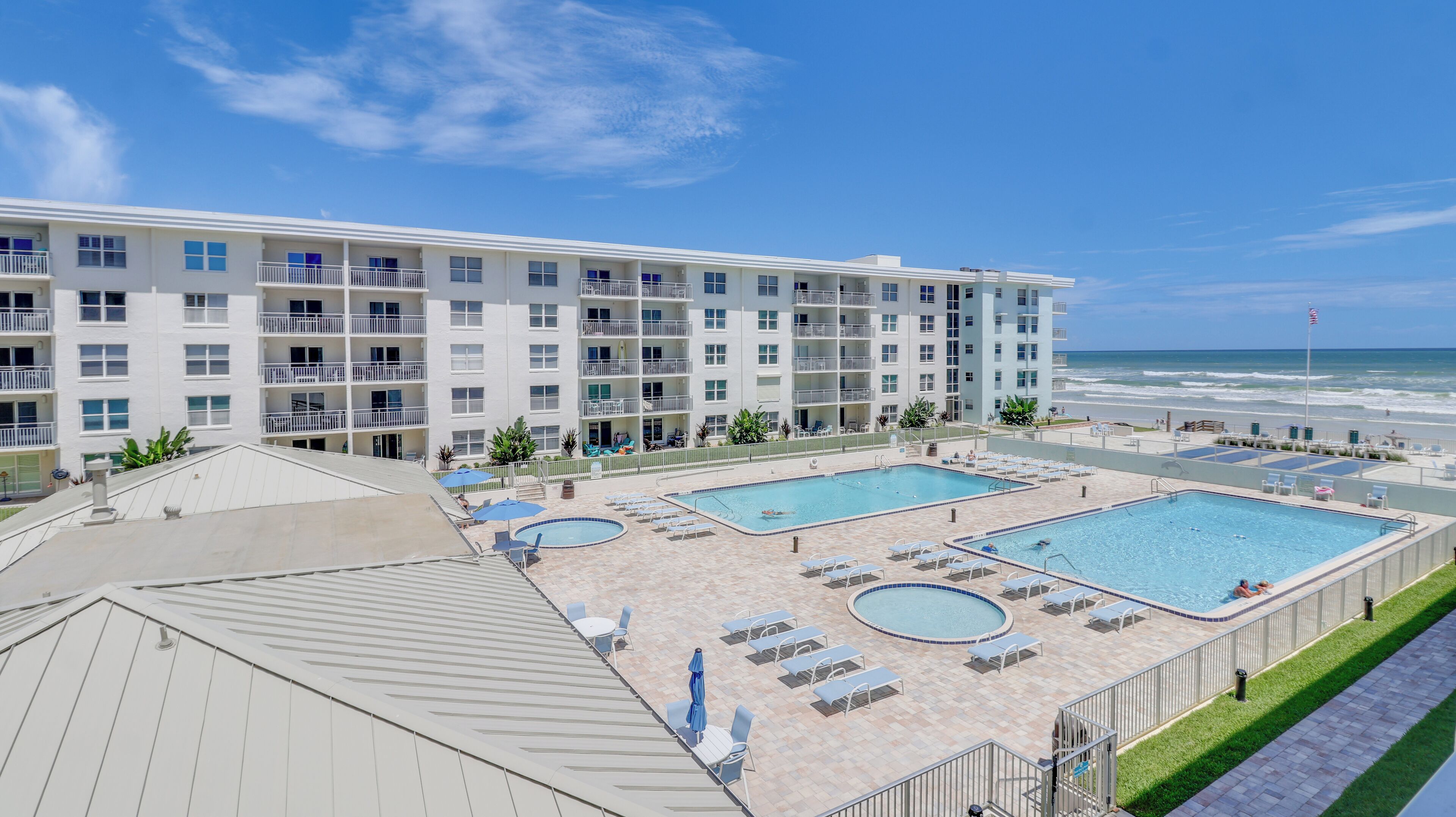 A hotel with multiple swimming pools, a beach view, and a large building with balconies.
