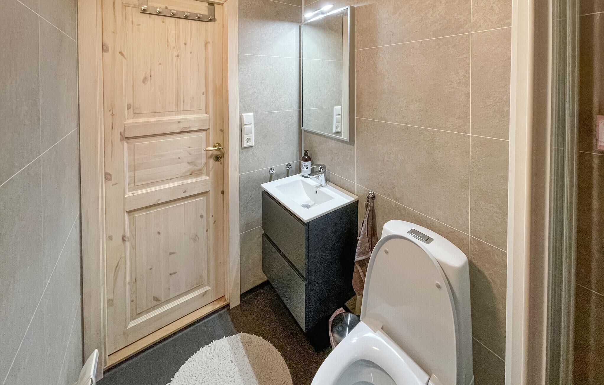 Ein kleines Badezimmer mit Holztür, Waschbecken, Spiegel und Toilette.