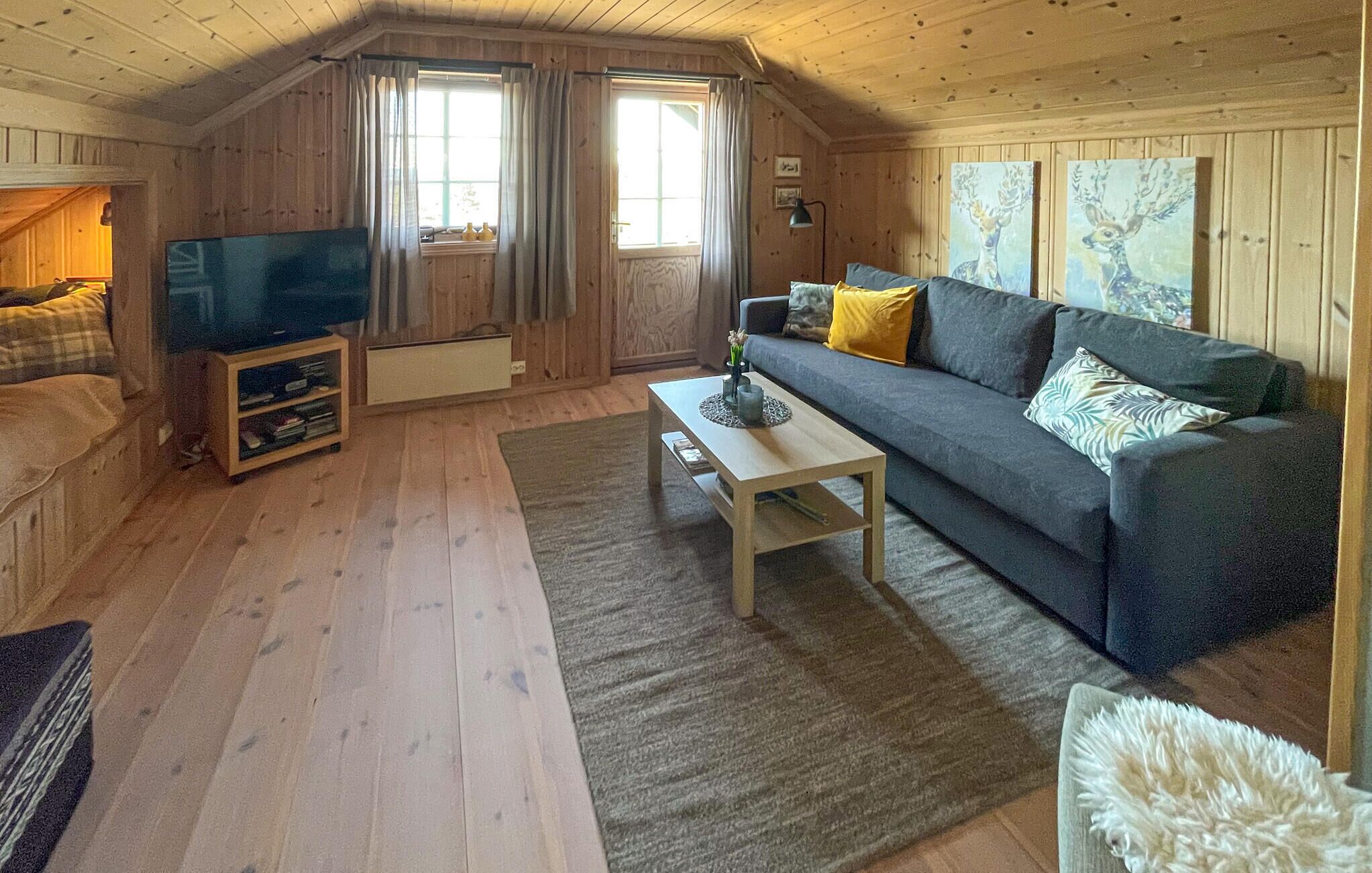 Et hyggeligt rum med træpaneler, en sofa, et fjernsyn og billedkunst på væggene.