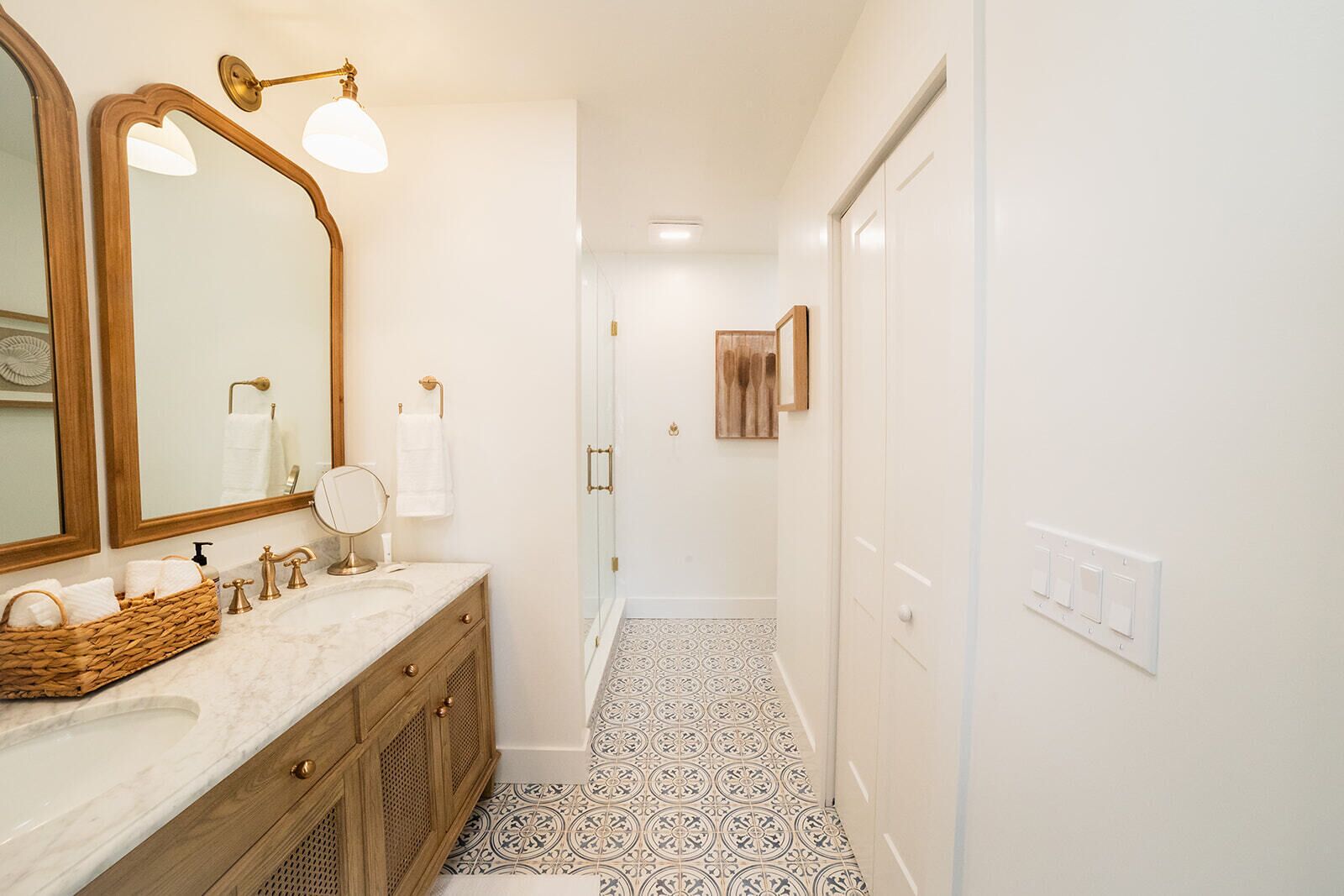 Une salle de bain dotée d’un comptoir en marbre, d’un grand miroir et d’un espace douche avec des carreaux à motifs.