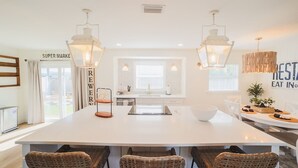 Una cocina moderna con una isla central, armarios blancos y sillas de mimbre.
