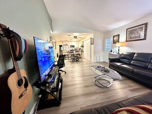 Een woonkamer met een televisie, een gitaar, een bank en een salontafel.