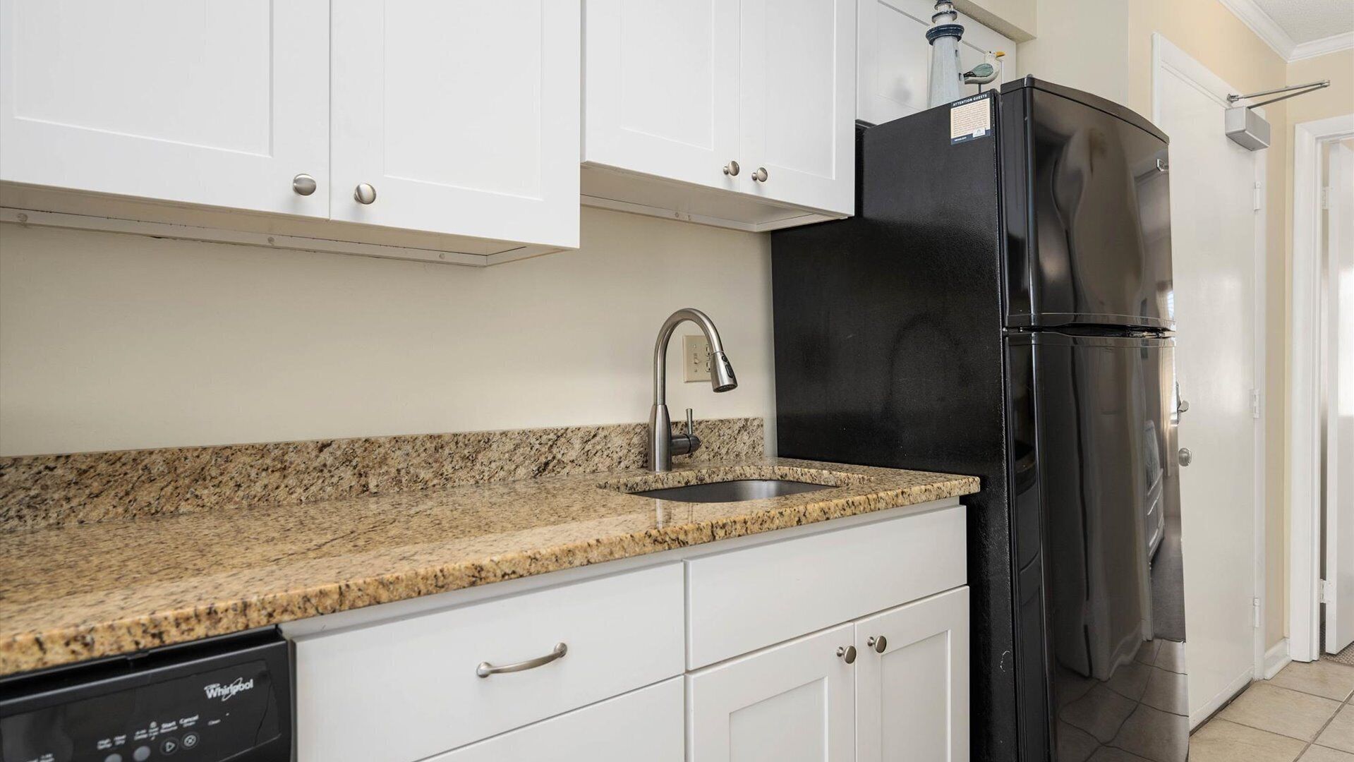A kitchen with white cabinets, a granite countertop, a stainless steel sink, and a black refrigerator.
