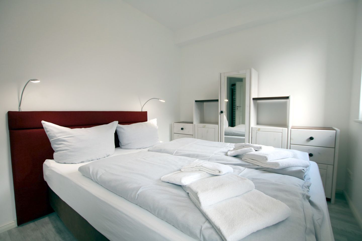 Habitación de hotel moderna con una cama grande, ropa de cama blanca, cabecera roja y un espejo sobre la cama.