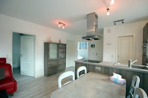 Une cuisine moderne avec un îlot central, des chaises blanches et un canapé rouge dans l’espace salon.