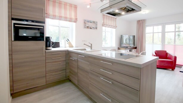 A modern kitchen with a built-in oven, a coffee maker, and a large island with a sink. - Strandstraße 18c, Whg. 7, Haus Paul - Ferienwohnung mit 3- Zimmern auf ca. 70m² im EG mit Terrasse (Wyk auf Föhr)