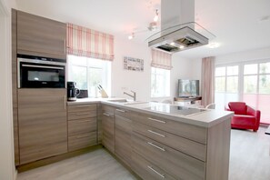 A modern kitchen with a built-in oven, a coffee maker, and a large island with a sink. - Strandstraße 18c, Whg. 7, Haus Paul - Ferienwohnung mit 3- Zimmern auf ca. 70m² im EG mit Terrasse (Wyk auf Föhr)
