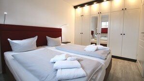 A hotel room with a large bed, a red headboard, white bedding, a bedside table with a lamp, and a wardrobe with mirrors. - Strandstraße 18c, Whg. 7, Haus Paul - Ferienwohnung mit 3- Zimmern auf ca. 70m² im EG mit Terrasse (Wyk auf Föhr)