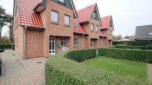 A multi-story brick building with a red-tiled roof, a paved driveway, and well-maintained hedges. - Strandstraße 18c, Whg. 7, Haus Paul - Ferienwohnung mit 3- Zimmern auf ca. 70m² im EG mit Terrasse (Wyk auf Föhr)