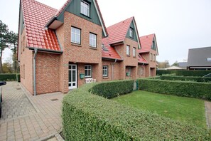 Een meerlaags bakstenen gebouw met een rode dakbedekking, een verharde oprit en goed onderhouden hagen.
